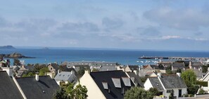 A coastal town with houses, a lighthouse, and boats in the harbor. - Quiet vacation rental with an exceptional ocean view in the hills above Erquy, Tu Est Roc + Park (Erquy)