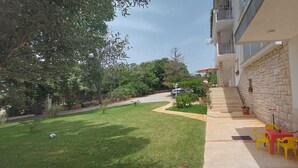 A modern building with a stone facade, a small outdoor seating area with yellow and red chairs, and a well-maintained lawn. - HAWAII One-Bedroom Apartment 7 (Banjole)