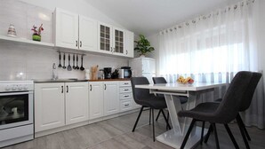 A modern kitchen with white cabinets, a dining table with chairs, and a refrigerator. - HAWAII One-Bedroom Apartment 7 (Banjole)