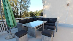 Un balcón con muebles de mimbre, que incluye una mesa con superficie de vidrio y asientos acolchados.