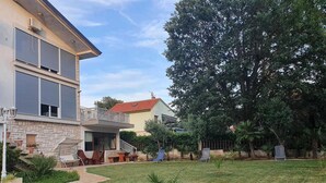Una casa de dos pisos con un balcón, un jardín con césped y plantas en macetas, y una valla.