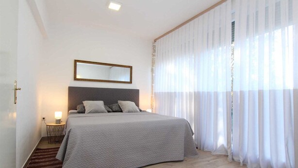 Un dormitorio con una cama grande, una mesita de noche, un espejo y cortinas de gasa.
