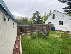 Ein Garten mit eingezäuntem Bereich, einem kleinen Patio-Tisch und Stühlen.