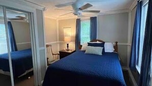 A hotel room with a large bed, a ceiling fan, a nightstand, and a window with curtains. - Homey Houghton Haven (Roscommon)