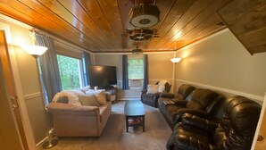 A living room with a sofa, a black leather couch, a TV, and a ceiling fan. - Homey Houghton Haven (Roscommon)