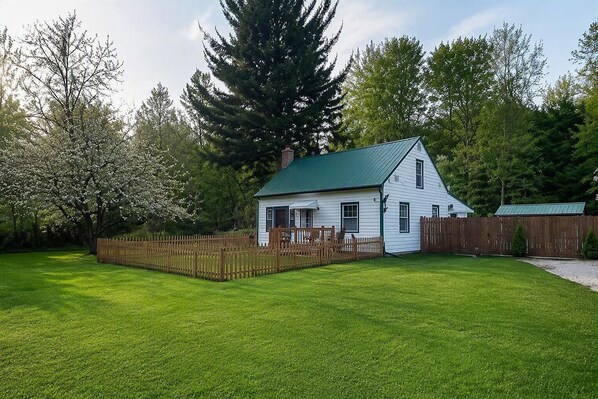 Een wit huis met een groen dak, omgeven door een houten omheining en een verzorgd gazon.