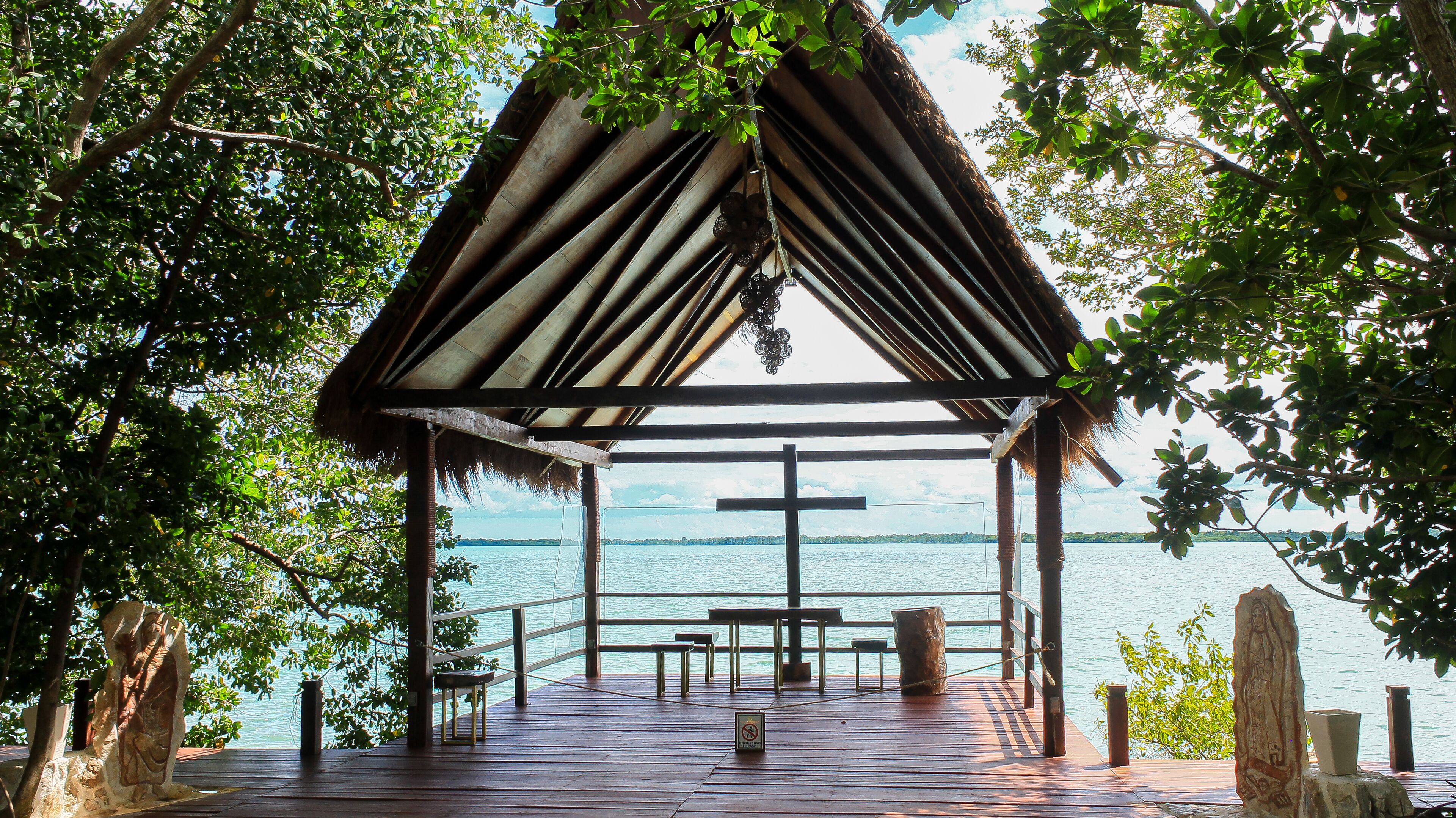 A wooden deck with benches and a thatched-roof pavilion overlooking a body of water.