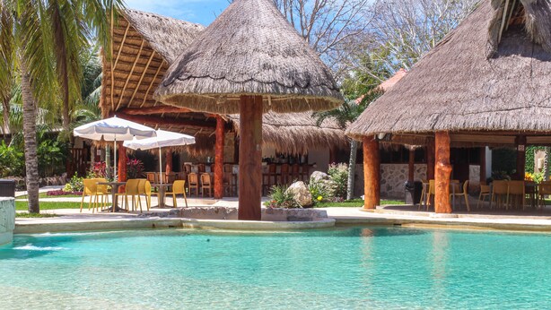 A pool area with thatched-roof structures, outdoor seating, and a clear blue pool. - Villa Marcela (Chetumal)