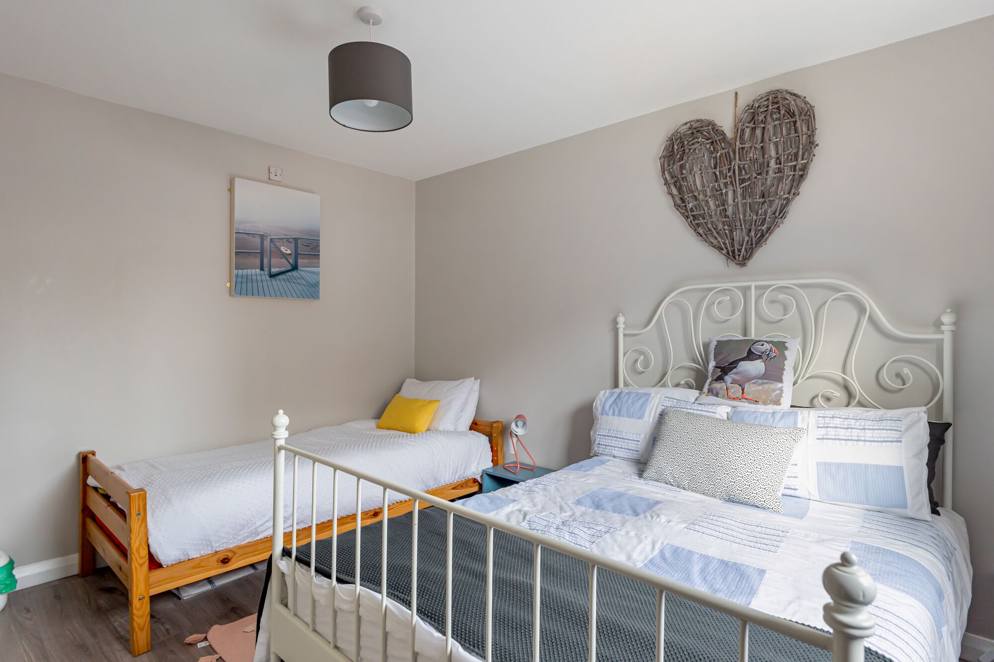 Quarto com duas camas de solteiro, um coração decorativo na parede e um quadro emoldurado sobre uma das camas.