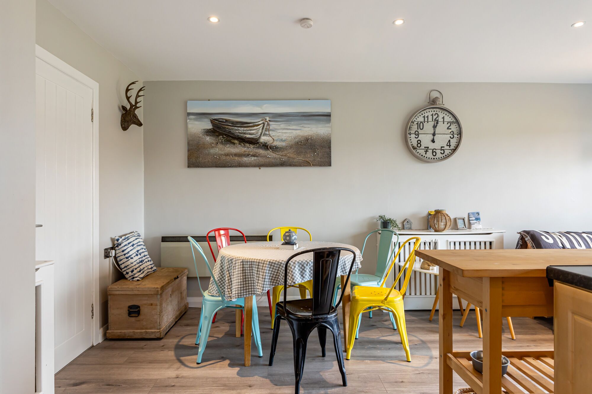 A dining area with a table, chairs, a clock, and a painting on the wall.