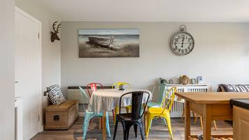 A dining area with a table, chairs, a clock, and a painting on the wall.