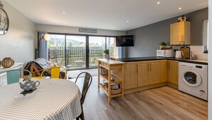 A modern kitchen with wooden cabinets, a built-in washing machine, and a dining area with a table and chairs. - Central Apartment 3B (Newcastle)