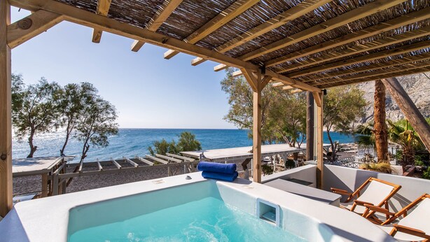 Un espace piscine avec vue sur la mer, des chaises longues en bois et une structure en forme de pergola.