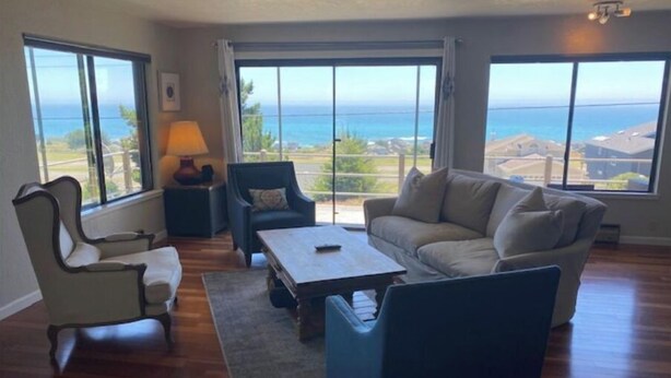 Een woonkamer met uitzicht op de oceaan, met een bank, een fauteuil, een salontafel en een lamp.