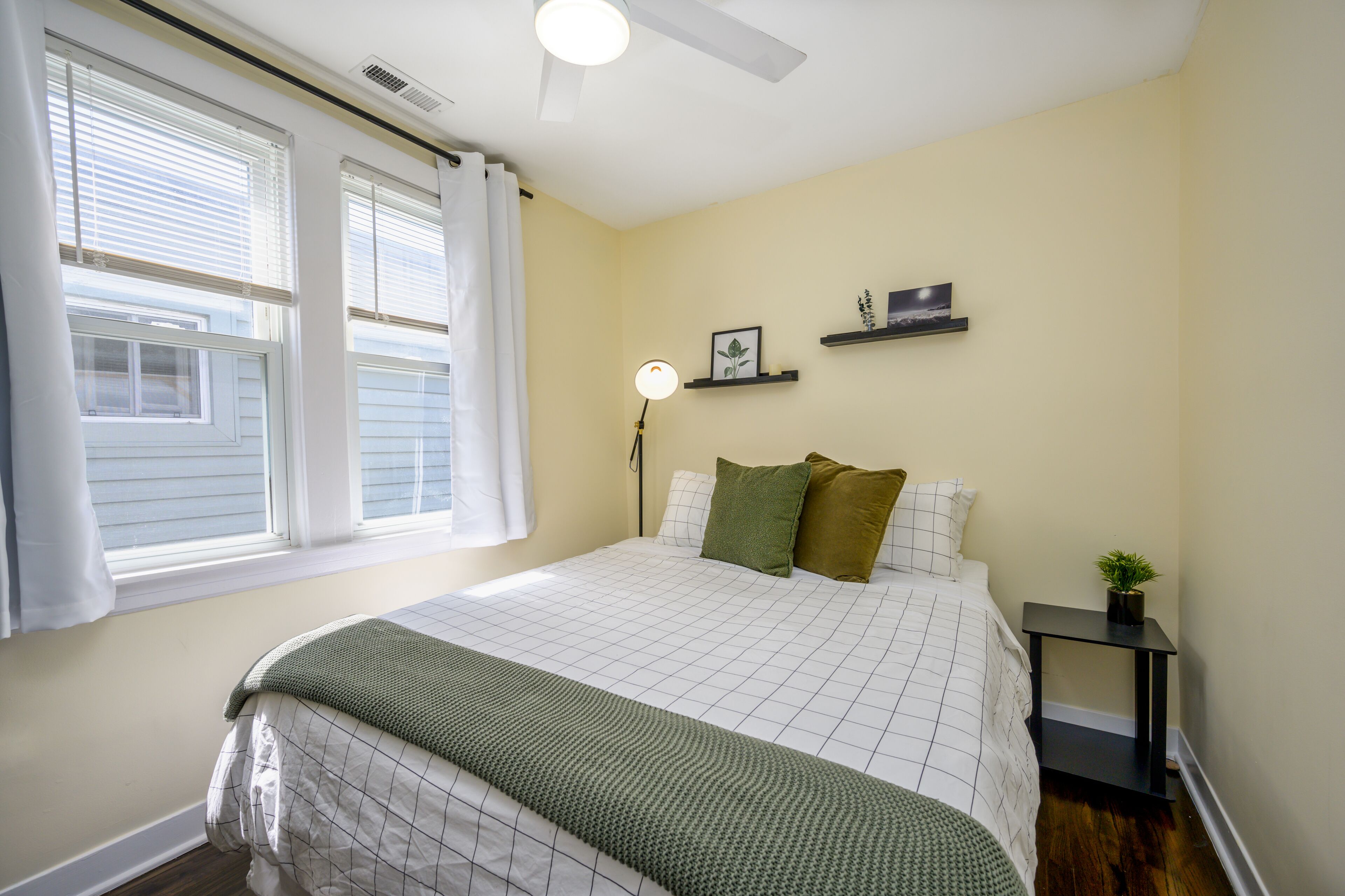 A bedroom with a bed, a bedside table with a lamp, and a window with blinds.