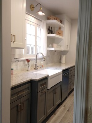 A modern kitchen with white cabinetry, a marble countertop, and a built-in dishwasher.