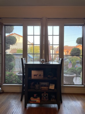 Una habitación con piso de madera, una mesa de madera oscura con superficie de vidrio y una ventana con vista a un barrio.