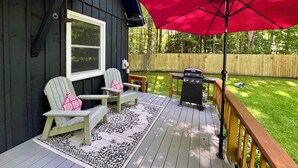 Une terrasse avec deux fauteuils Adirondack, un barbecue et un parasol rouge.