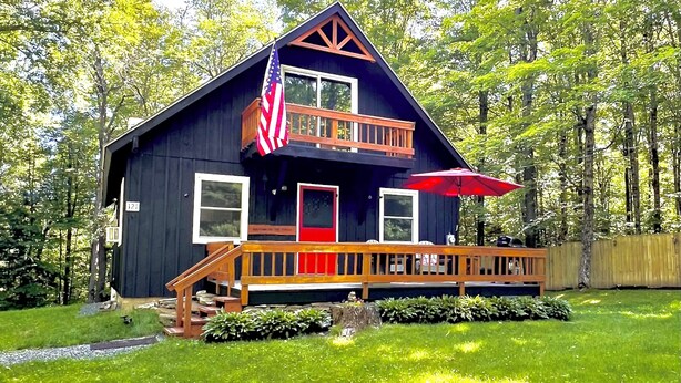 Une cabane avec une terrasse en bois, une porte rouge et un drapeau américain.