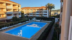 Una piscina rodeada de setos bien cuidados y bancos blancos, con edificios de varios pisos al fondo.