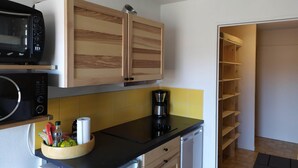 Una cocina compacta con armarios de madera, microondas, cafetera y lavavajillas.