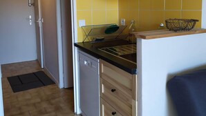 Una cocina compacta con armarios de madera, encimera negra y salpicadero de azulejos amarillos.