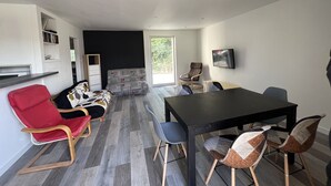 A modern living room with a black sofa, red armchair, and a dining table with chairs.