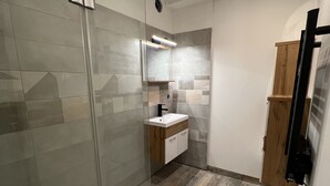 A modern bathroom with a glass shower enclosure, a wooden vanity, and a tiled floor.