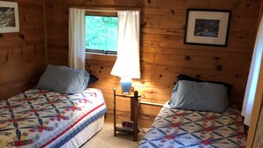 Ein Cabin-Zimmer mit zwei Betten, einem Nachttisch mit Lampe, einer Uhr und einem Fenster mit Vorhängen.