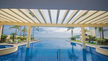 A pool area with a view of the ocean, palm trees, and a covered walkway.