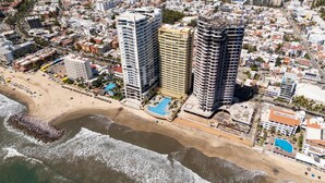 Luftaufnahme einer Küstenstadt mit Hochhäusern, einem Strand und einem Schwimmbad.
