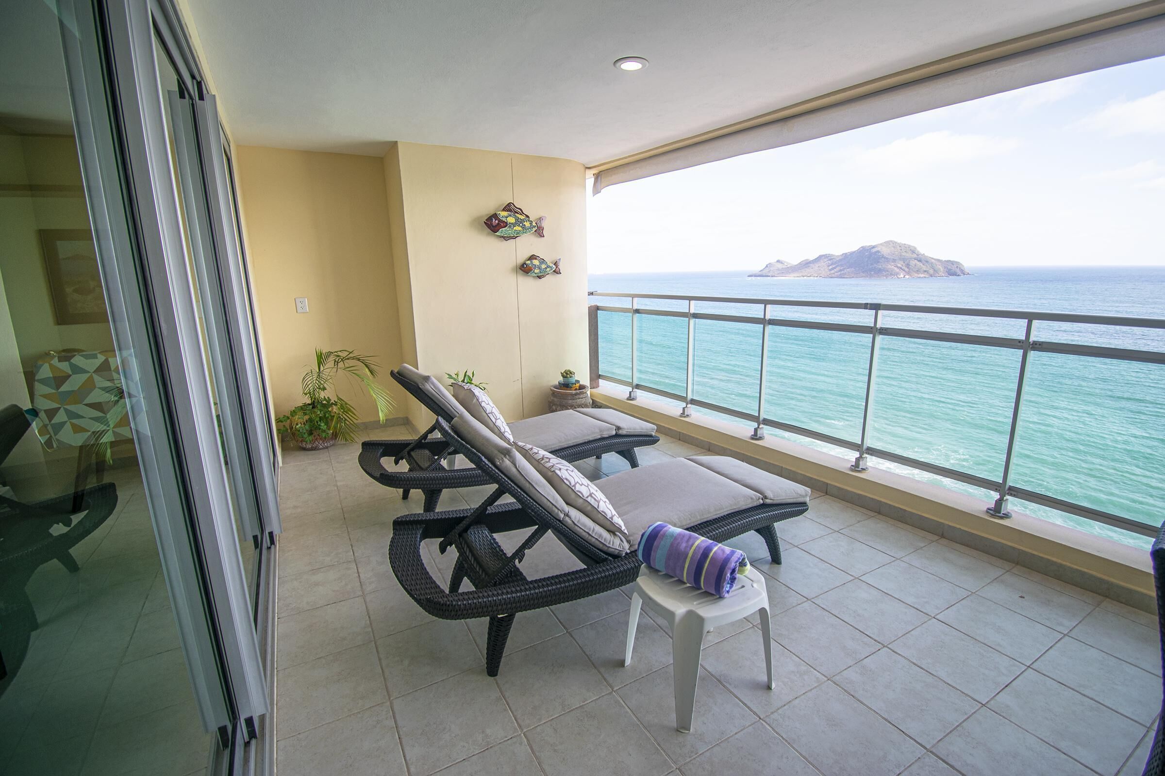 A balcony with two lounge chairs, a small table, and a potted plant.