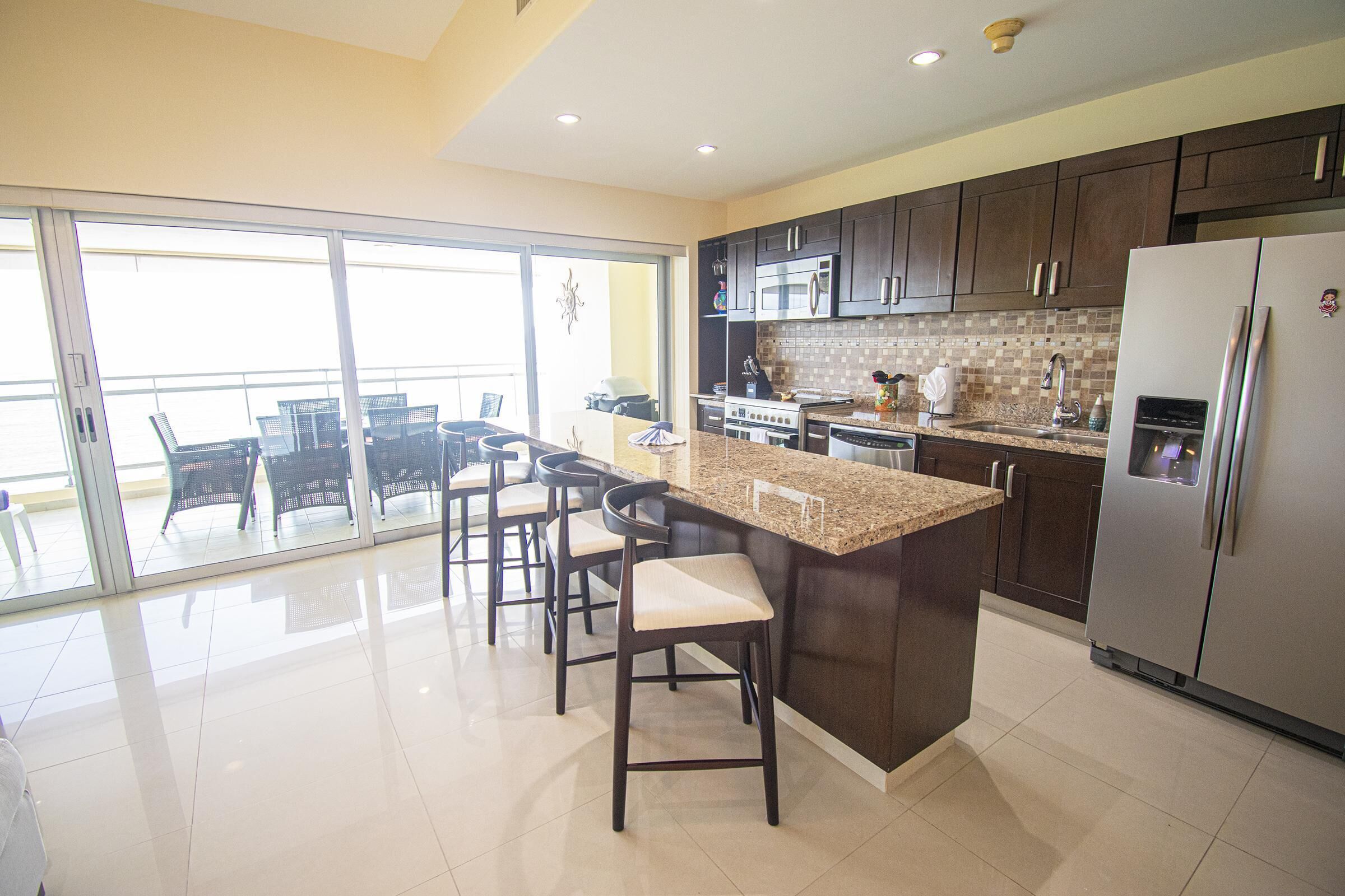 A modern kitchen with dark cabinets, a large island, and a stainless steel refrigerator.