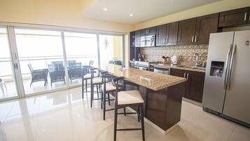 A modern kitchen with dark cabinets, a large island, and a stainless steel refrigerator.