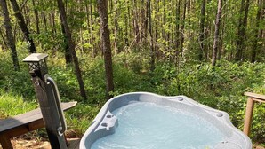 Un jacuzzi en zona boscosa con asientos de madera y abundante vegetación.
