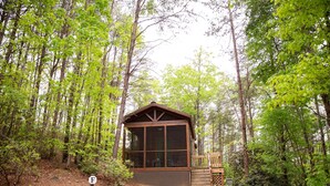 Una cabaña pequeña con un ventanal grande, rodeada de un bosque frondoso.
