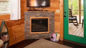 Interior de una cabaña de madera con chimenea, televisor y una puerta verde que da a una terraza.