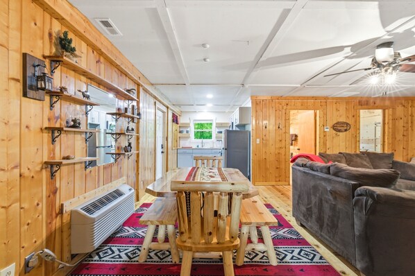 A wooden interior with a dining table, sofa, and shelves with various items.