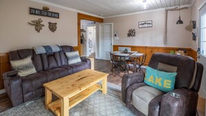 A cozy living room with a brown leather sofa, a wooden coffee table, and a dining area with a wooden table and chairs. - Hill Hideaway Unit 2 - Pet-Friendly Lake Retreat (Minocqua)