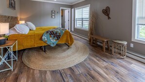 A bedroom with a bed, a round woven rug, a wooden bench, and a small stool. - Hill Hideaway Unit 2 - Pet-Friendly Lake Retreat (Minocqua)