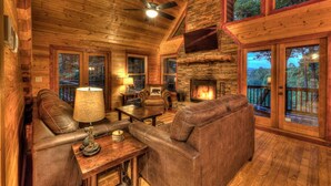 A cozy cabin interior with a fireplace, leather sofas, and a stone wall. - Aska Retreat - Pet Friendly | Hot Tub | Foosball | Arcade Games (Blue Ridge)