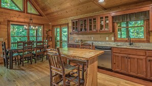 A wooden cabin interior with a dining area, kitchen, and large windows. - Aska Retreat - Pet Friendly | Hot Tub | Foosball | Arcade Games (Blue Ridge)
