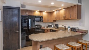 A modern kitchen with wooden cabinets, a stainless steel refrigerator, a microwave, a stove, a sink, and bar stools. - Westwind 407 (Vail)
