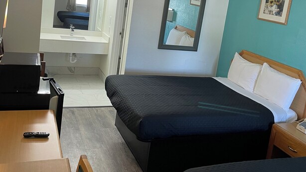A hotel room with a bed, a desk, a chair, a mirror, and a picture on the wall. - Executive Inn of Purcell (Purcell)