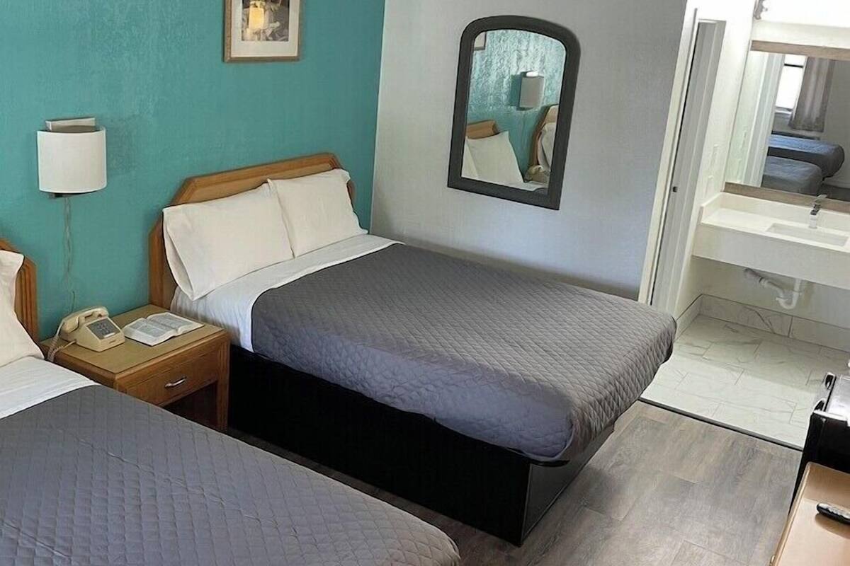 A hotel room with two beds, a bedside lamp, a telephone, a mirror, and a painting on the wall.