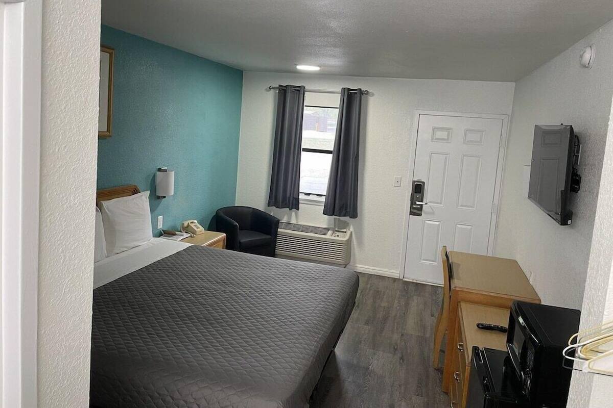 A hotel room with a bed, a desk, a chair, a television, and a window with curtains.