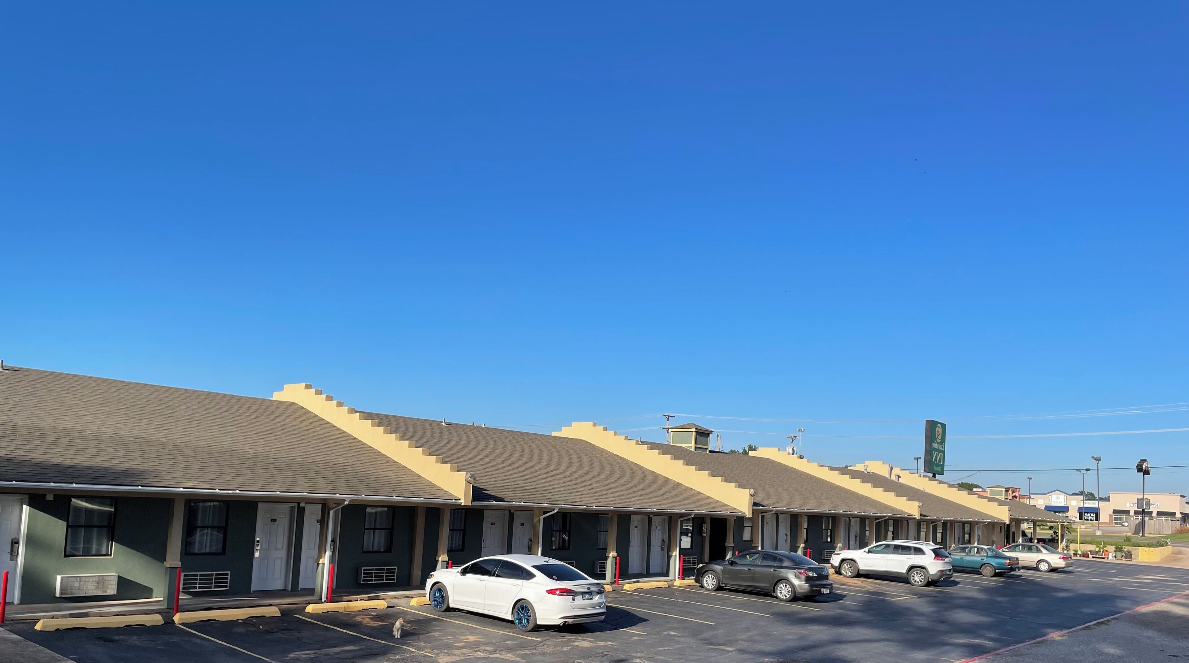 A row of motel buildings with a parking lot in front.