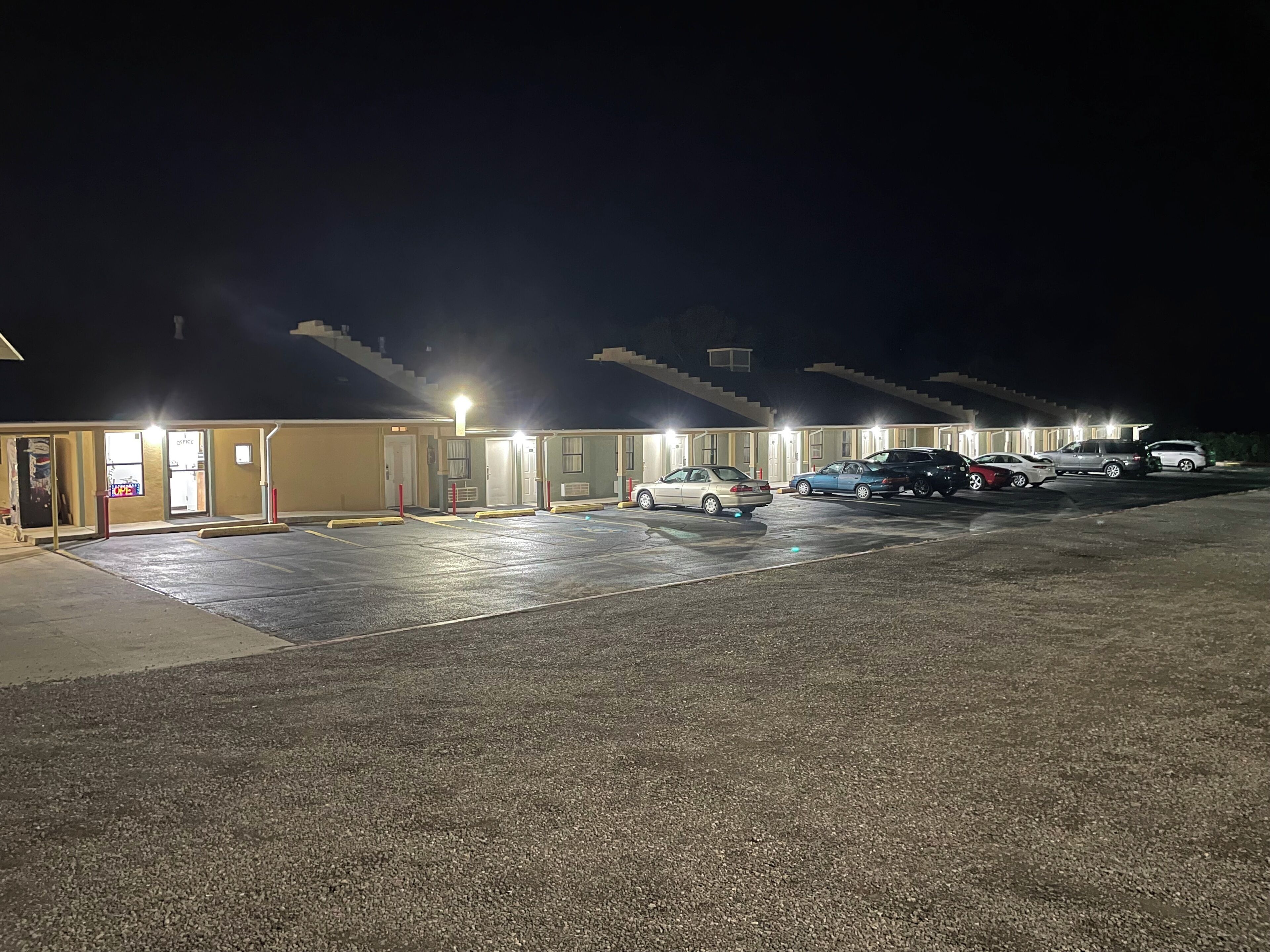 Um motel com vários quartos, estacionamento e uma escadaria que dá acesso ao andar superior.