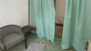 Une tente avec un tapis à motifs verts, une chaise en bois et un rideau suspendu.