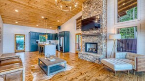 A spacious living area with a stone fireplace, wooden flooring, and a high ceiling with exposed beams. - Big Sky 2 - Hot tub & game room (Epworth)